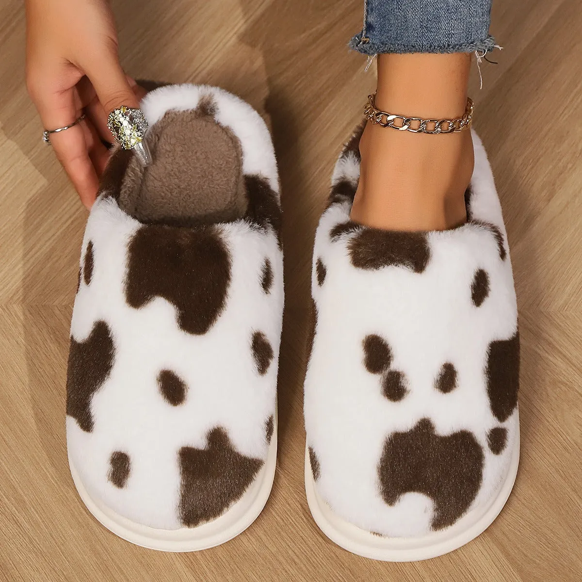 Cow spotted plush slippers in brown with round toe and baotou style on a home floor