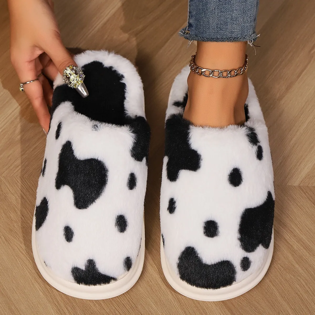 Cow spotted plush slippers in brown with round toe and baotou style on a home floor