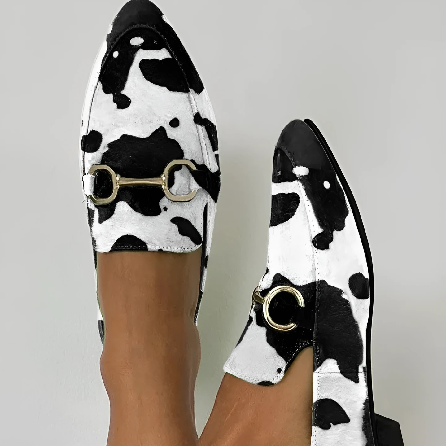 Women's black and white cow pattern pointed-toe mules with flat square heel on a neutral background