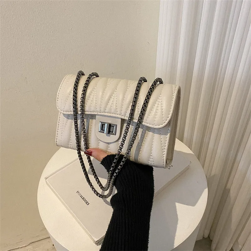 Small beige textured diamond pattern PU women's handbag with a soft handle on a table.