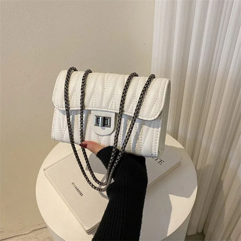 Small beige textured diamond pattern PU women's handbag with a soft handle on a table.