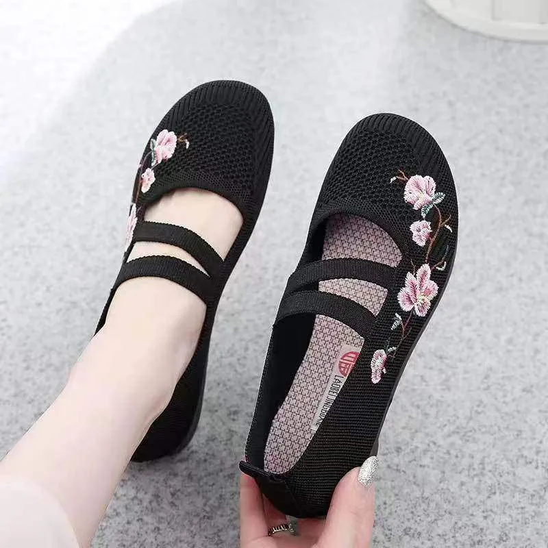 A pair of casual slip-on flat shoes with a round toe and elastic fabric upper, shown in an embroidered colour option.