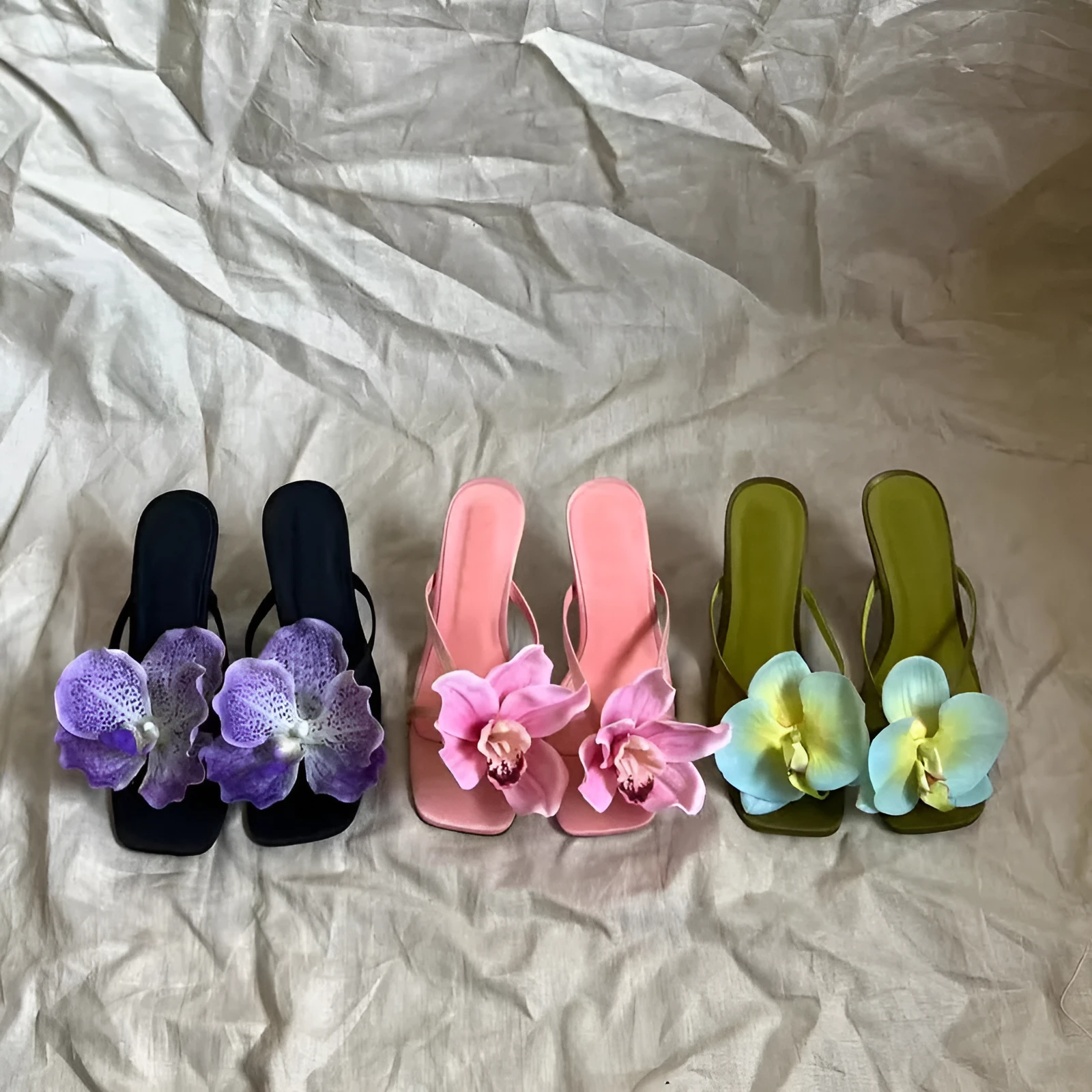 Pink women's sandals with a satin upper, artificial white Phalaenopsis flower, square toe, and a mid heel.