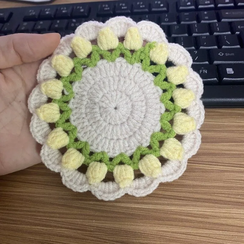 Handmade woven floral coaster in cotton and linen yarn on a wooden table