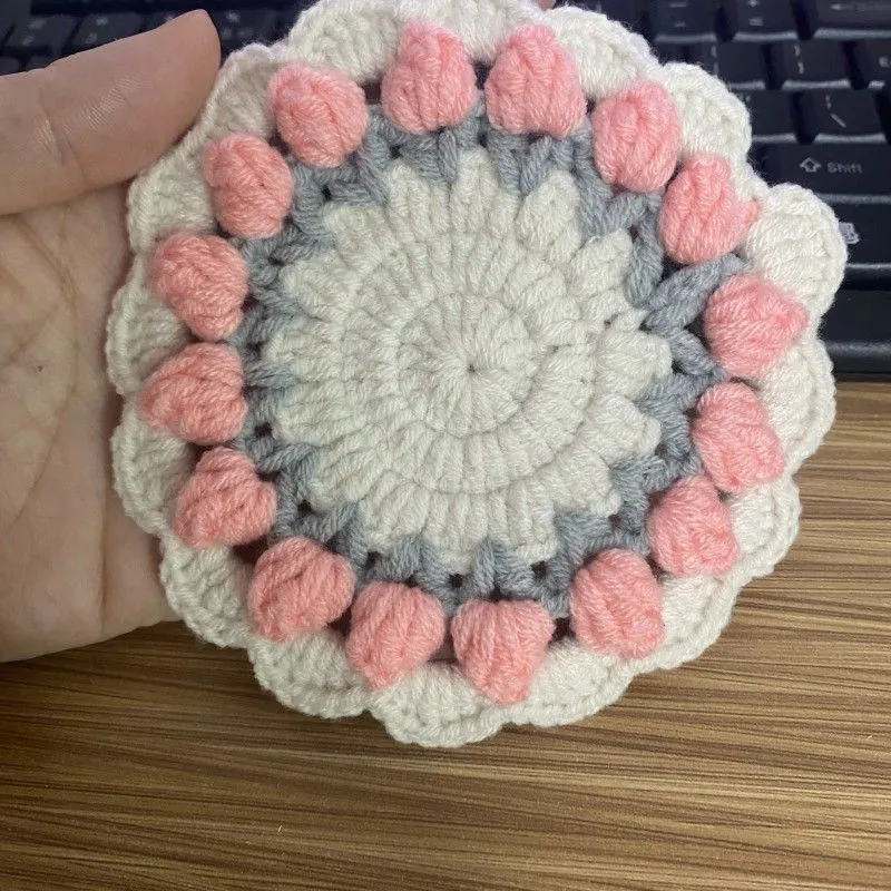 Handmade woven floral coaster in cotton and linen yarn on a wooden table