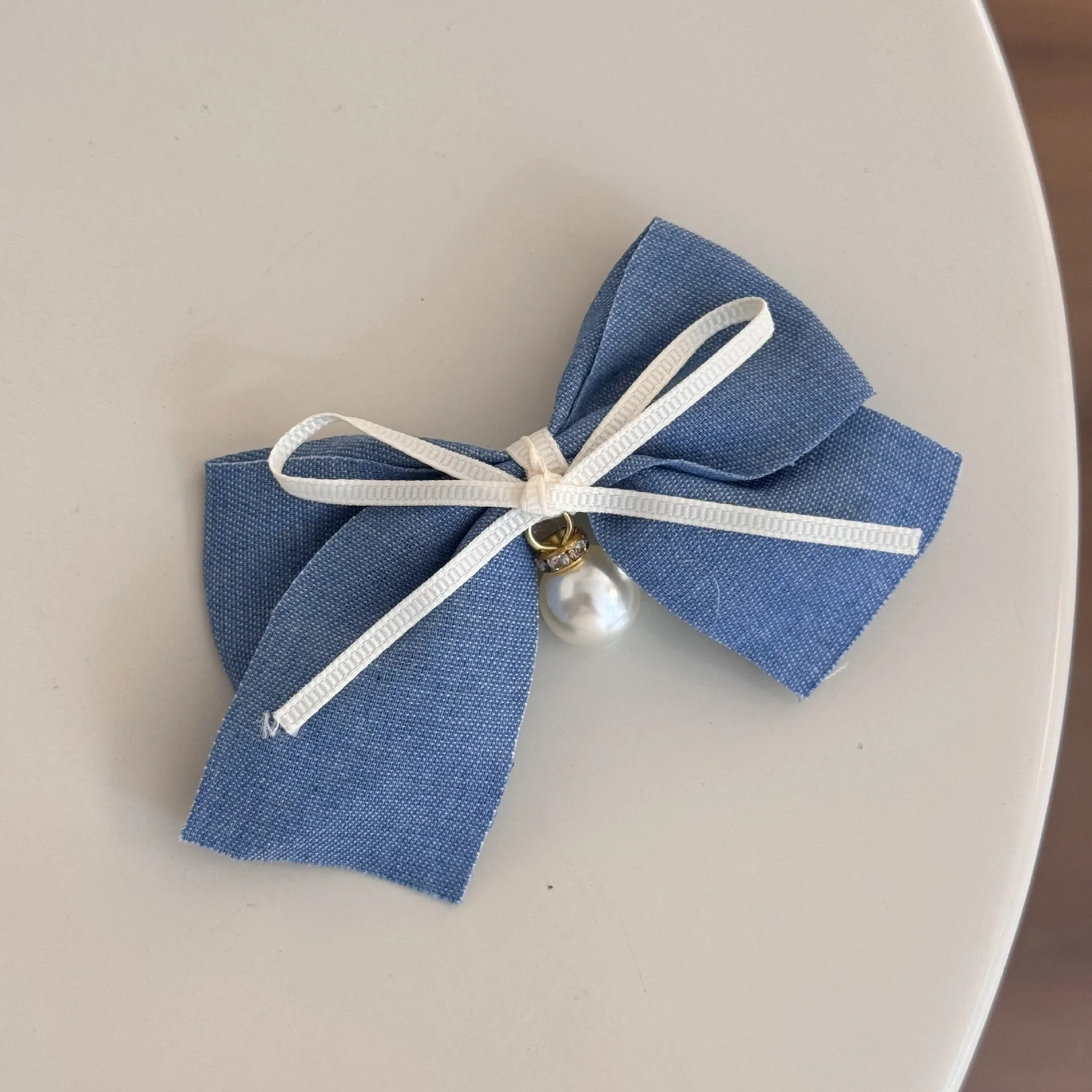 A women's hair clip barrette with a soft blue cloth bow and lace decoration on a plastic clip.