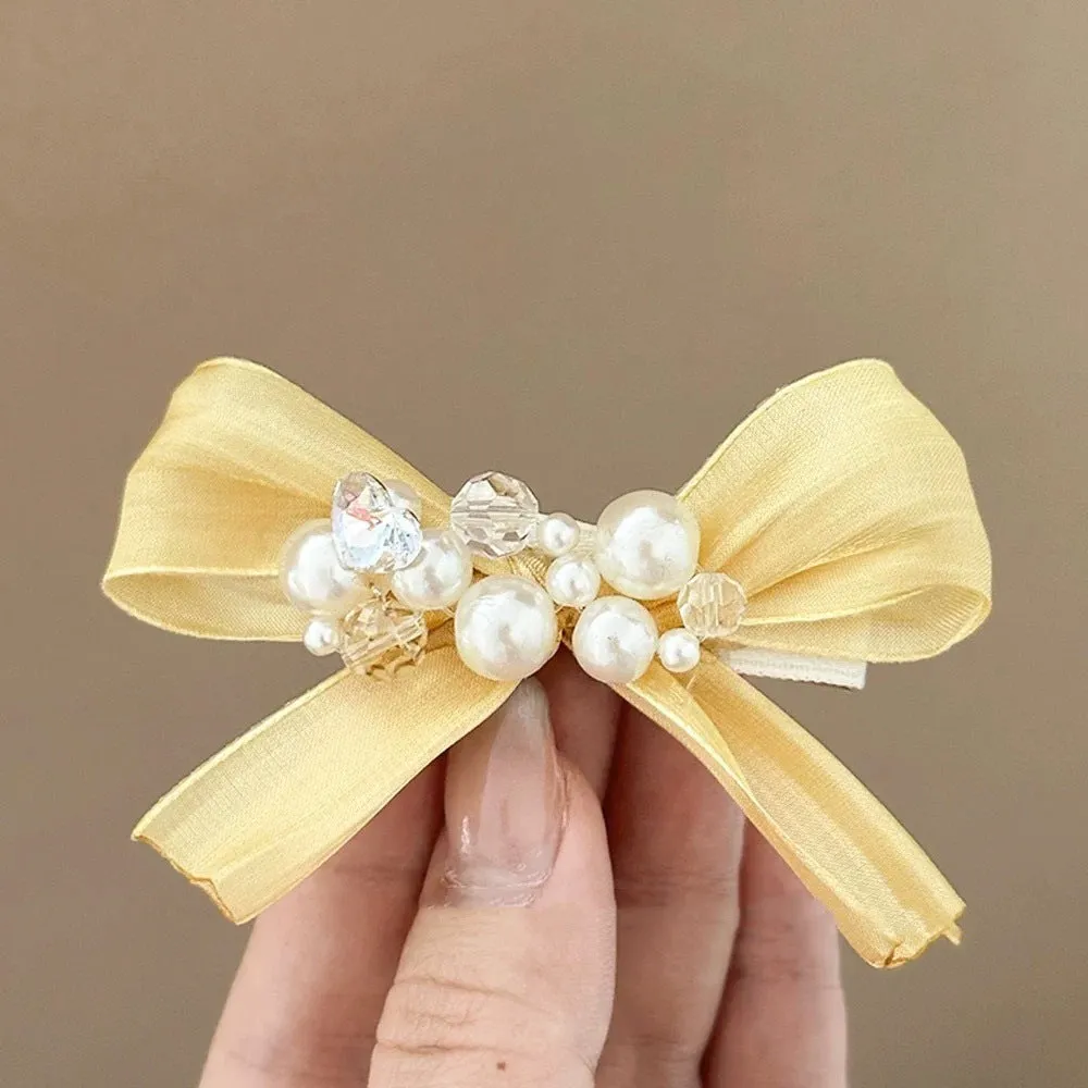 Yellow cloth bow barrette with rhinestones and a pearl on a plastic duckbill hair clip.