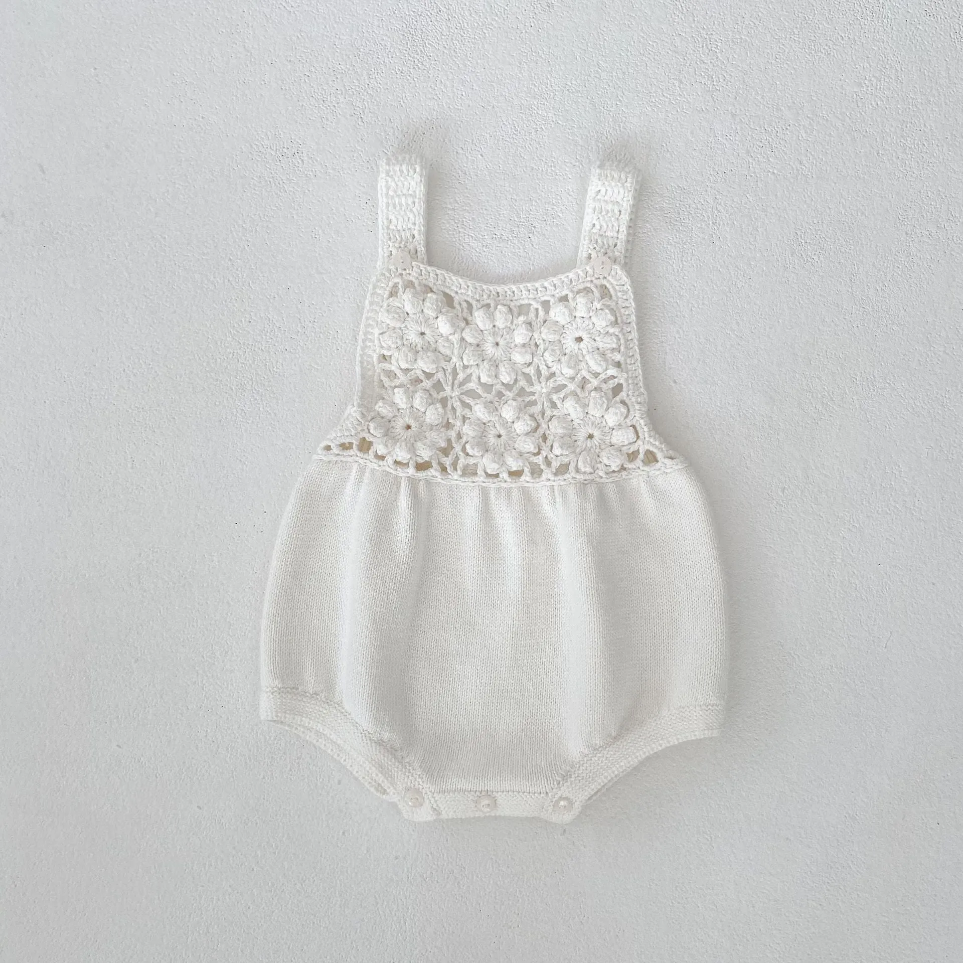 Beige baby romper with flower cutout strap and matching hat on a baby girl