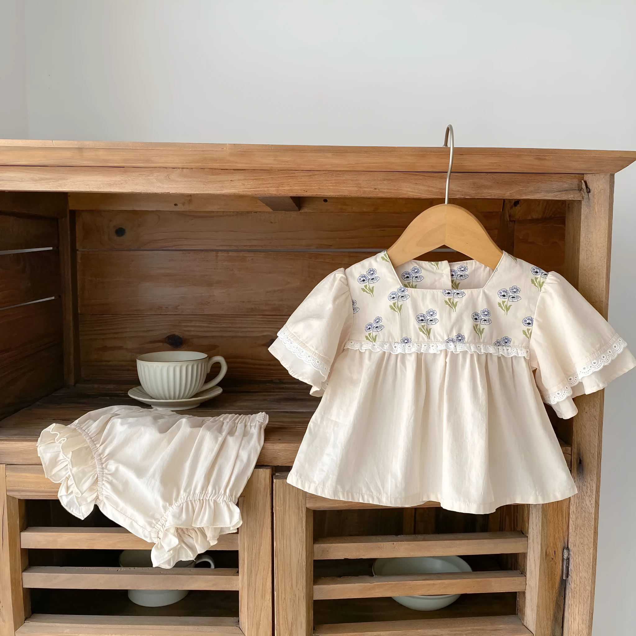 Apricot cotton two-piece suit with floral pattern, square collar top, and wooden horn buttons, next to matching bloomer pants.
