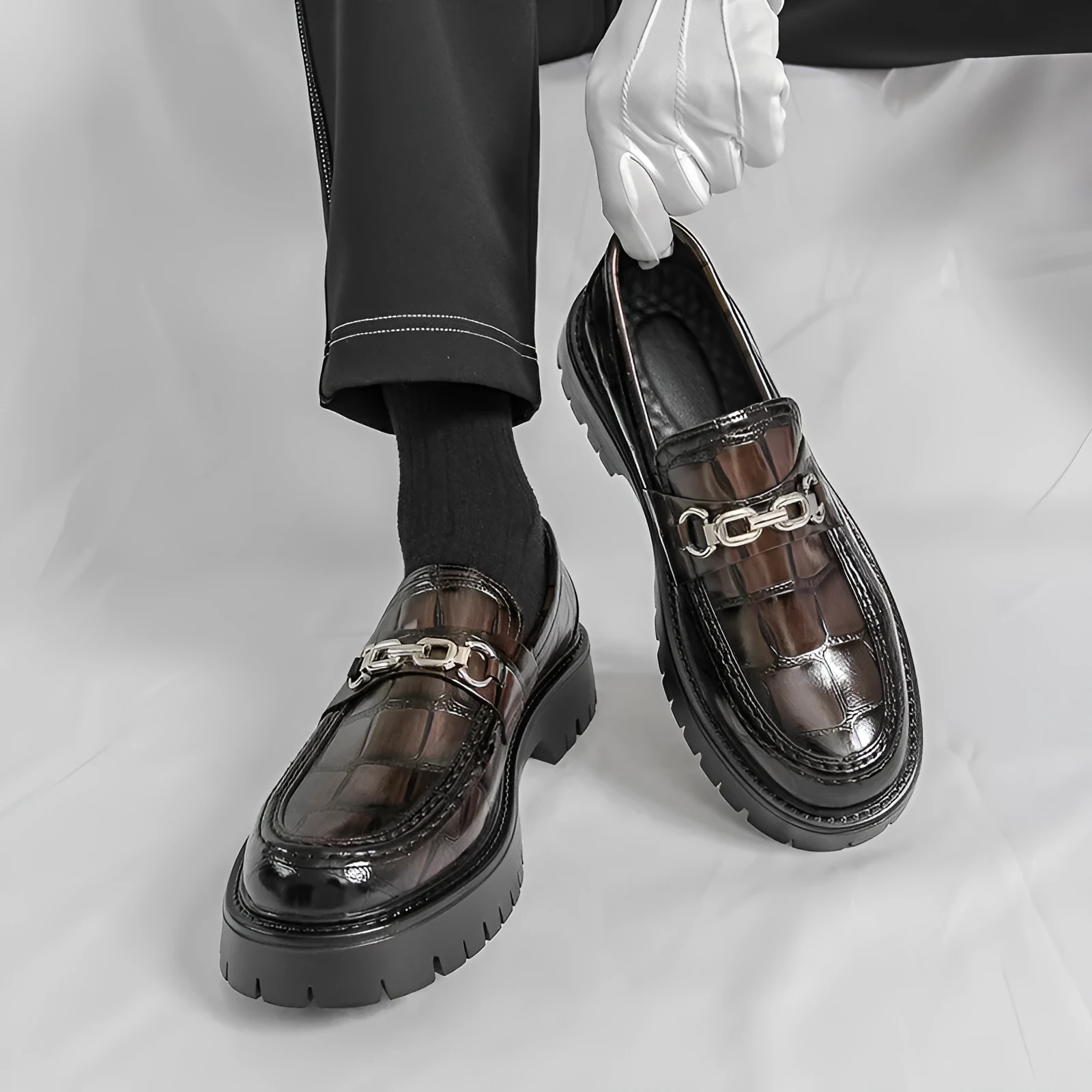 Men's black crocodile pattern loafers with a flat platform sole on a plain background.
