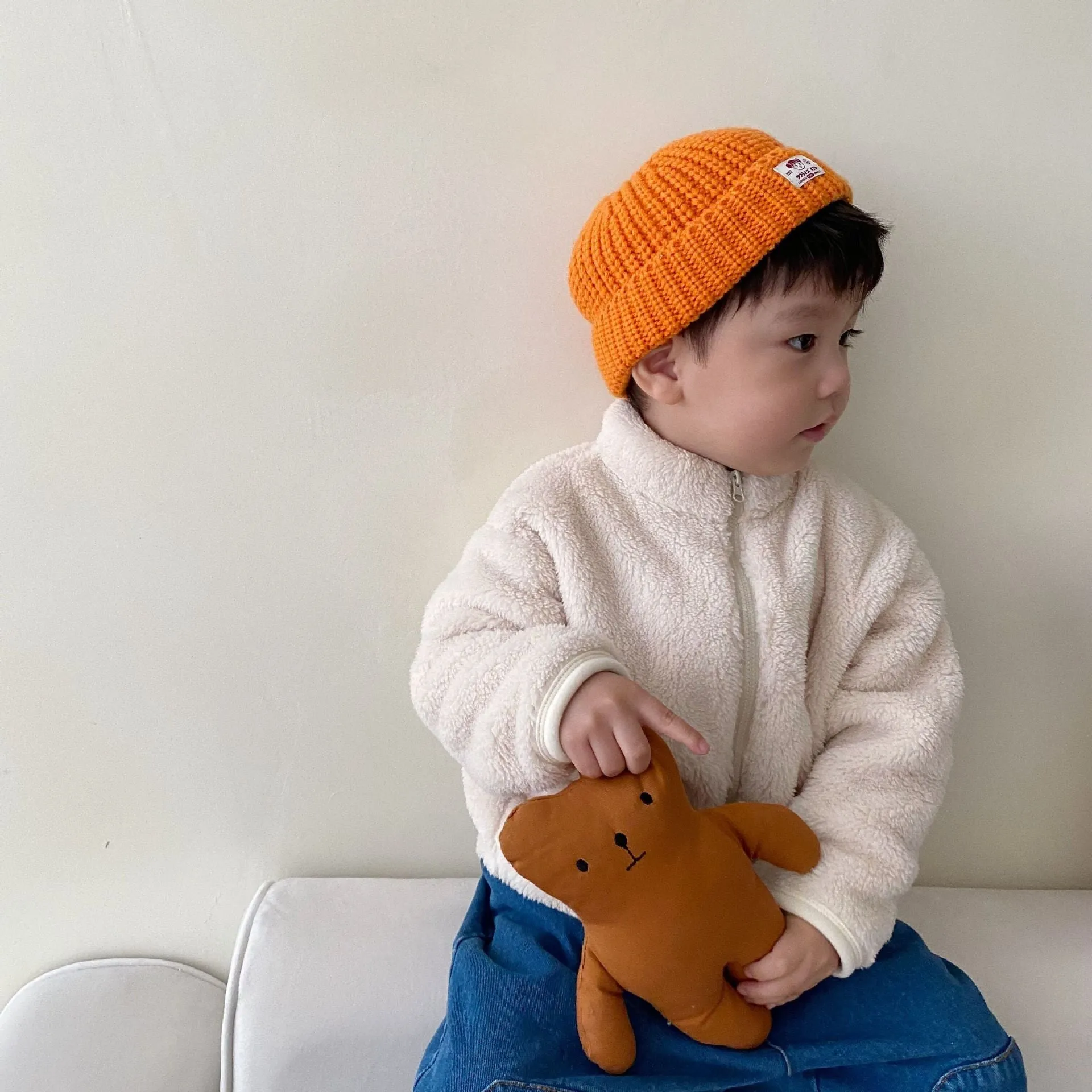 A child's blue sherpa fleece jacket with a full zip, high collar, and front pockets on a hanger.