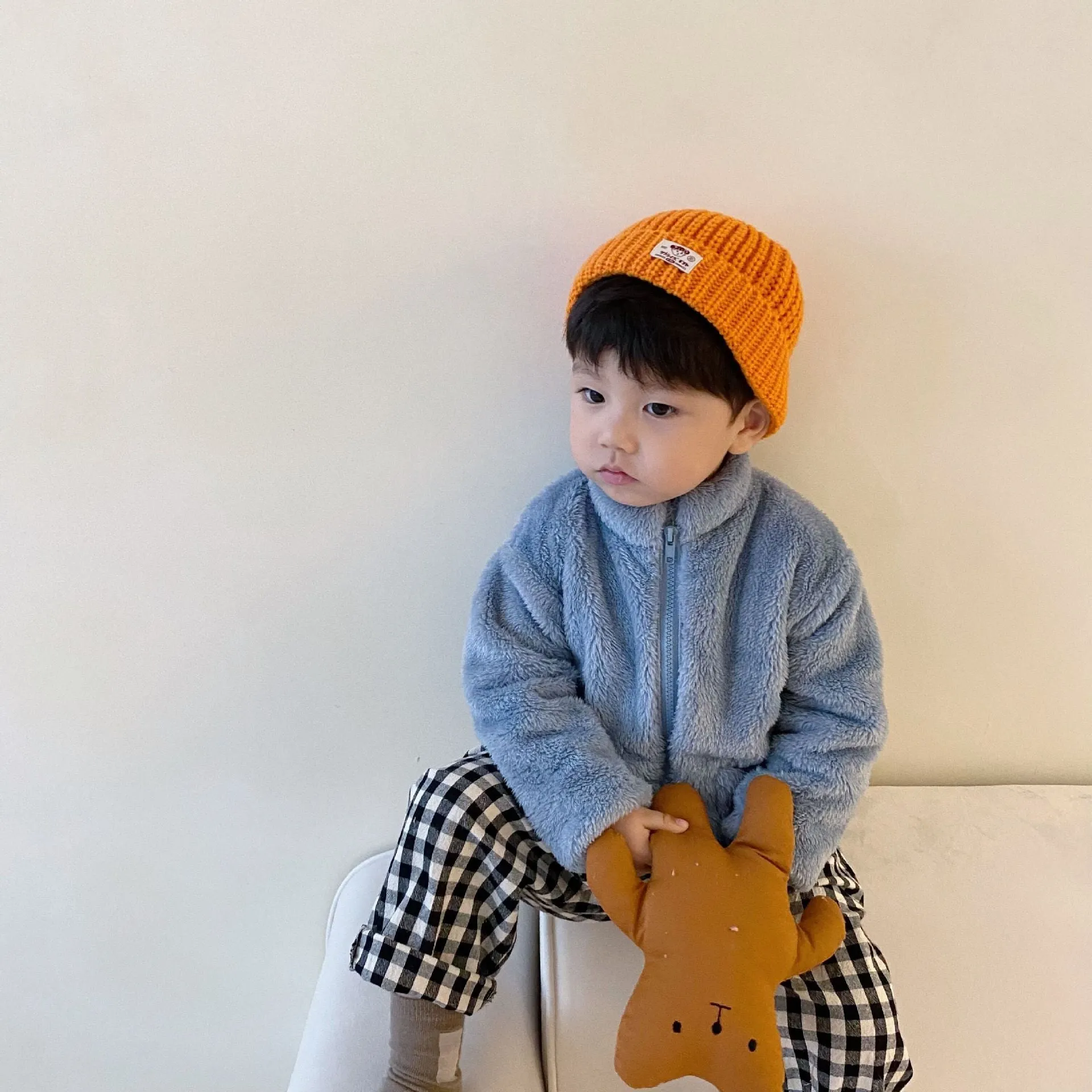 A child's blue sherpa fleece jacket with a full zip, high collar, and front pockets on a hanger.