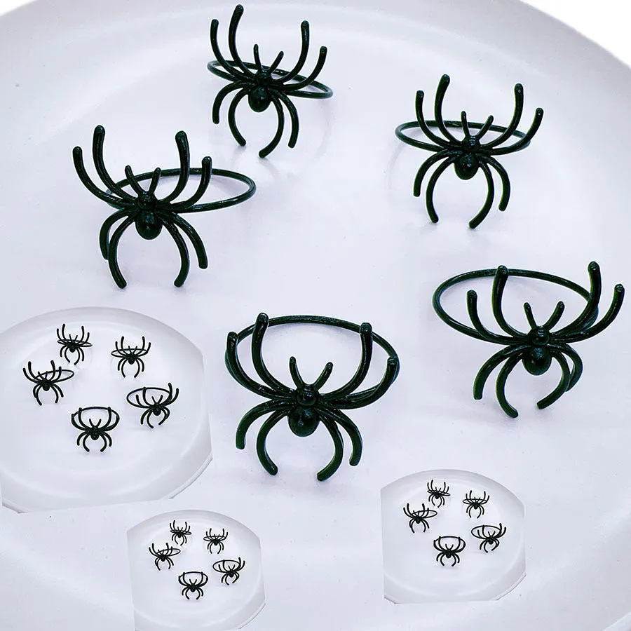 Set of six black alloy spider-shaped napkin rings on a dark tablecloth.
