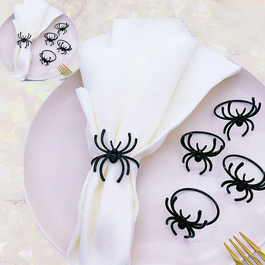 Set of six black alloy spider-shaped napkin rings on a dark tablecloth.