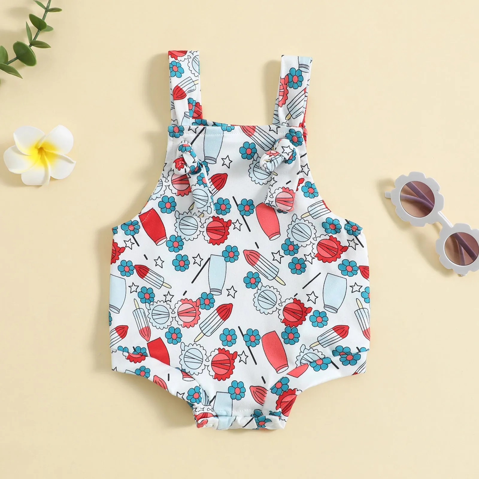 Baby girl wearing a sleeveless knotted front suspender pants jumpsuit in a printed design.