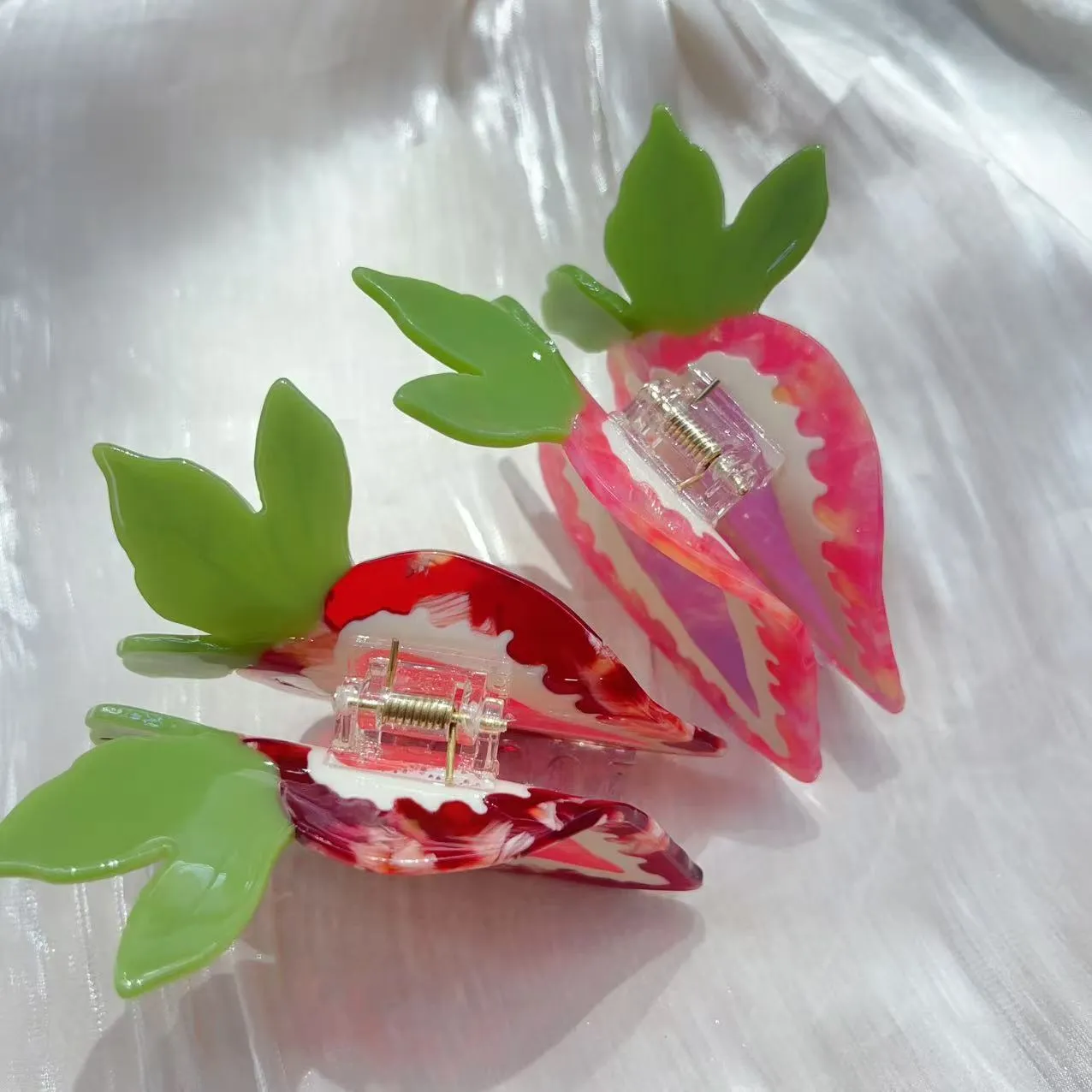 A close-up of a handmade strawberry-shaped hairpin in either red or pink colour on a light background.