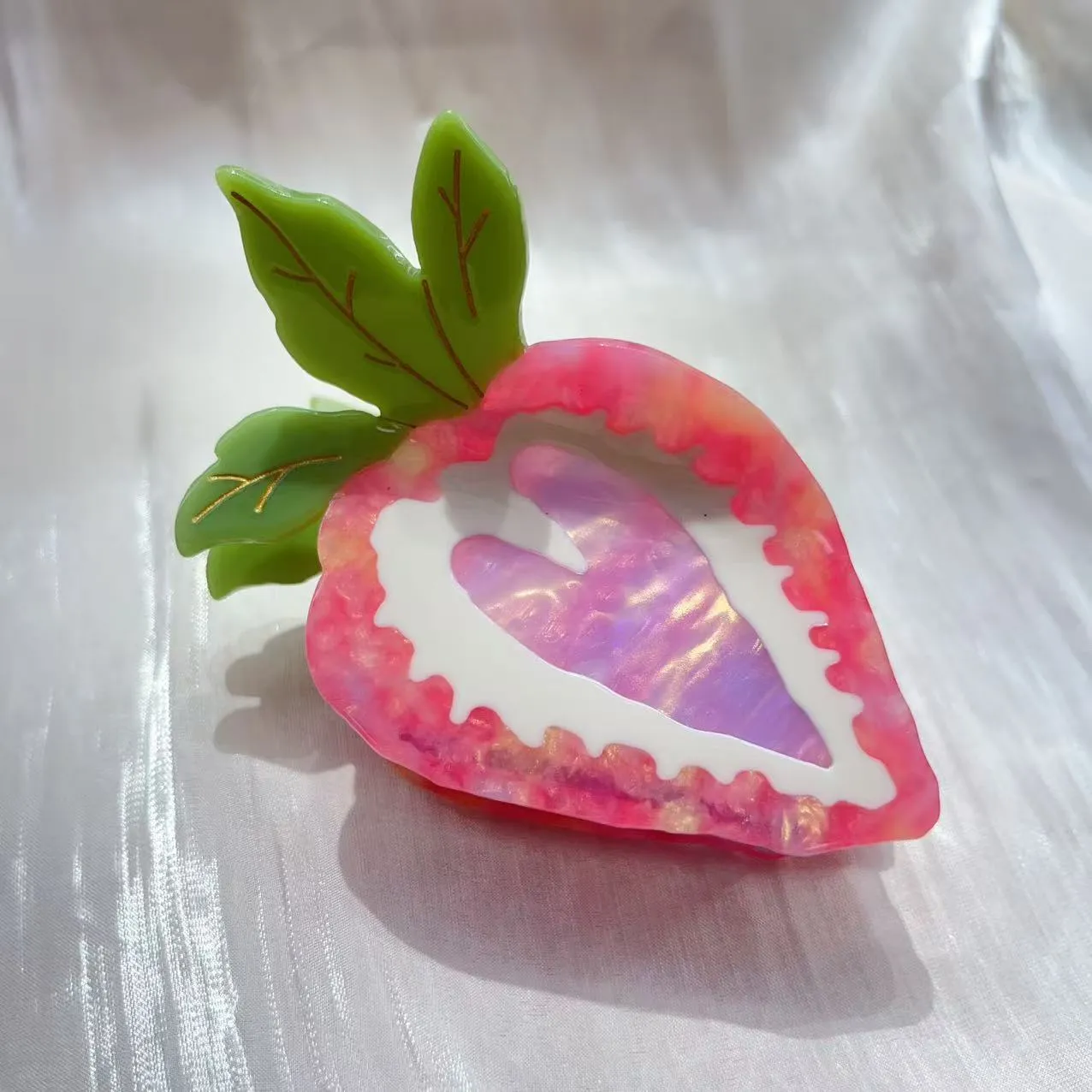 A close-up of a handmade strawberry-shaped hairpin in either red or pink colour on a light background.