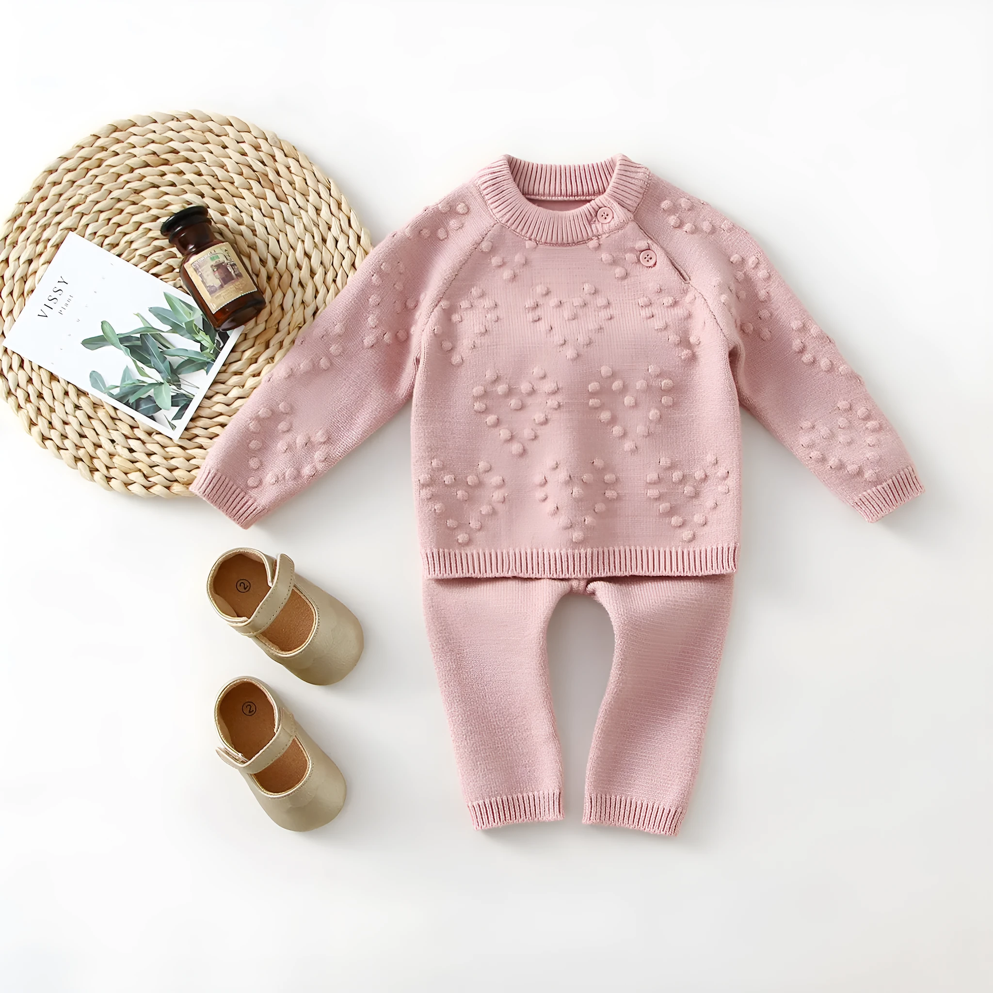 Baby girl wearing a pink knitted pullover sweater and matching trousers set.