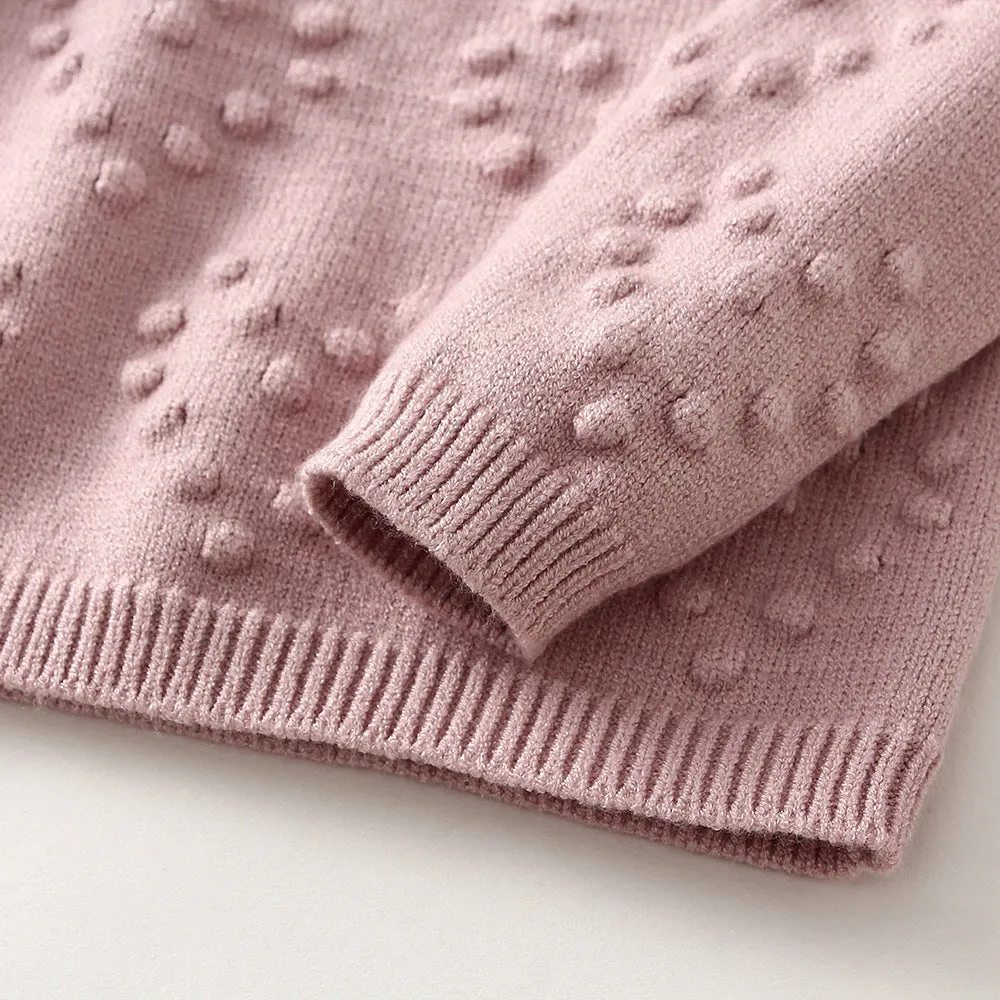 Baby girl wearing a pink knitted pullover sweater and matching trousers set.