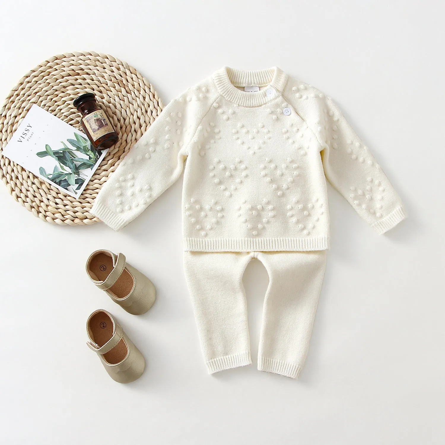 Baby girl wearing a pink knitted pullover sweater and matching trousers set.