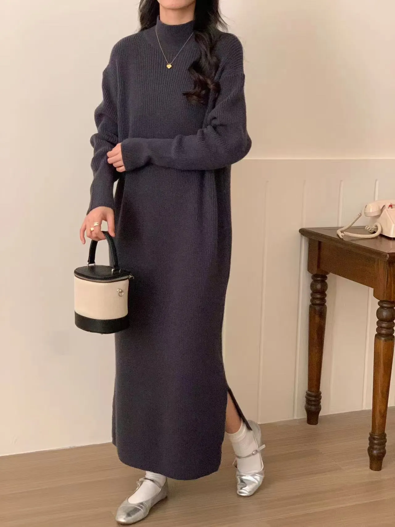 Woman wearing a milky white half turtleneck long sleeve knitted midi dress with a high waist.