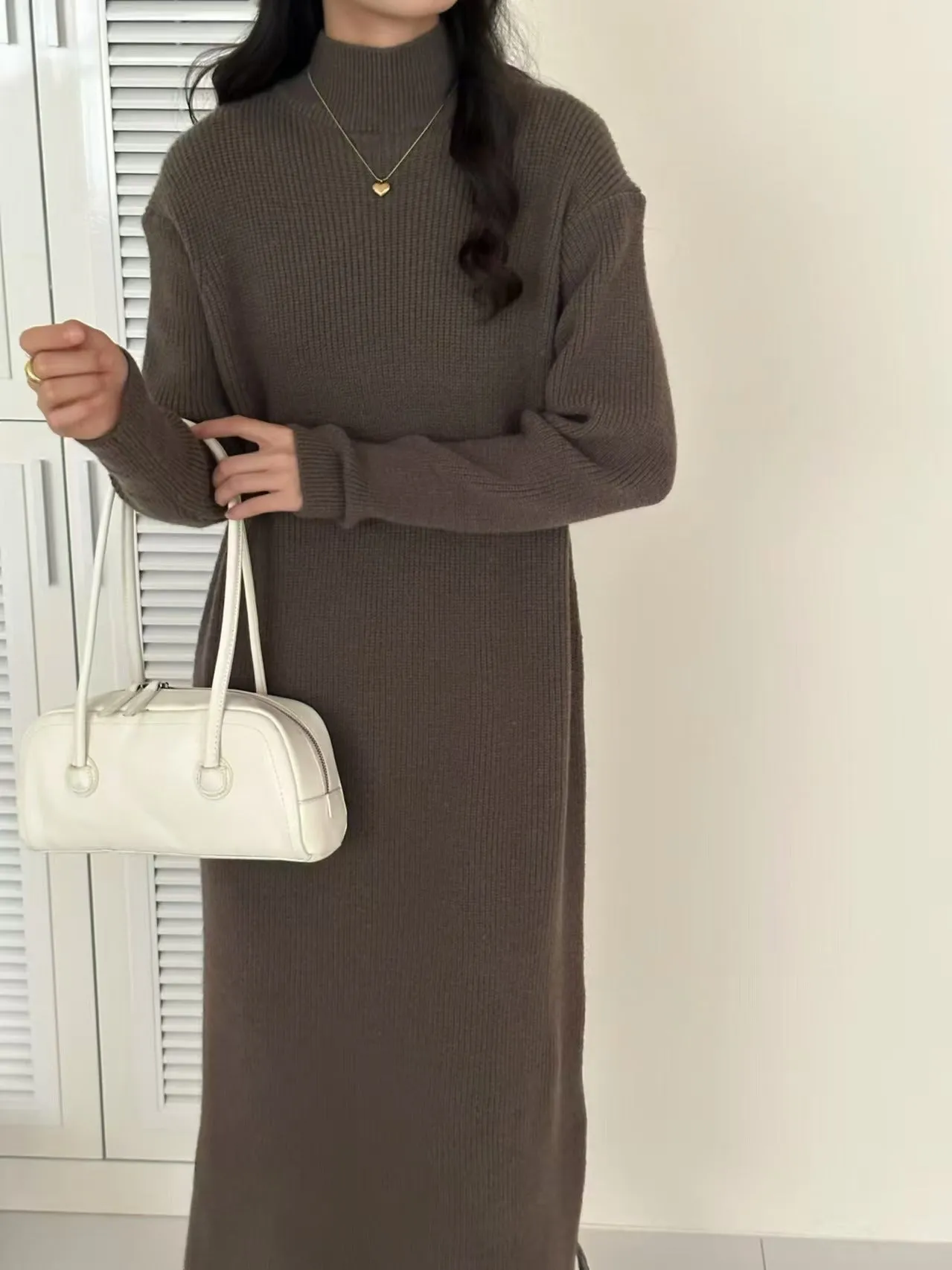 Woman wearing a milky white half turtleneck long sleeve knitted midi dress with a high waist.