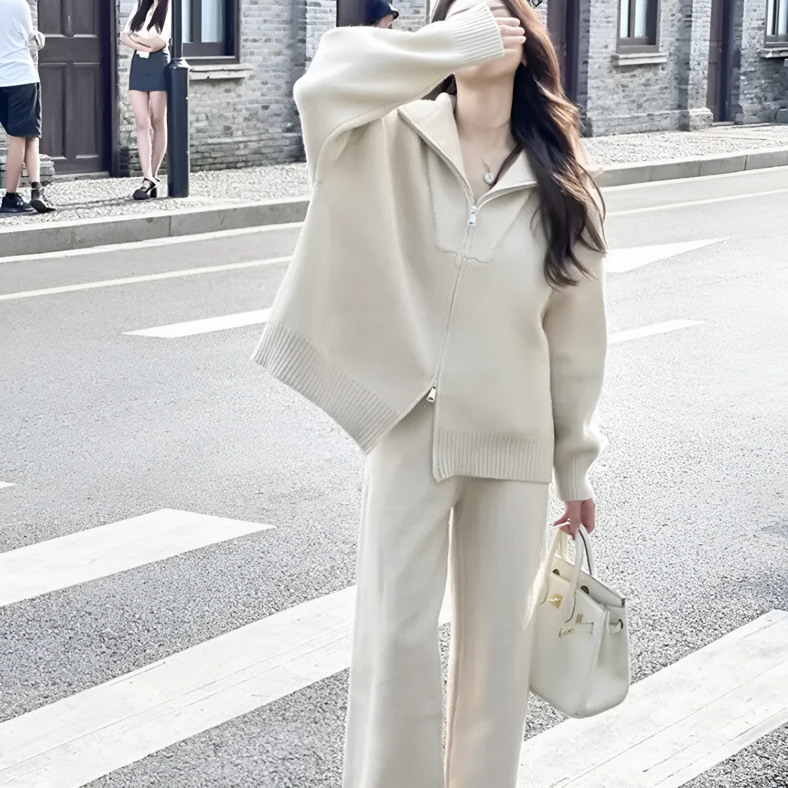 Woman wearing a knitted zipper cardigan and wide-leg trousers from a solid colour two-piece set.