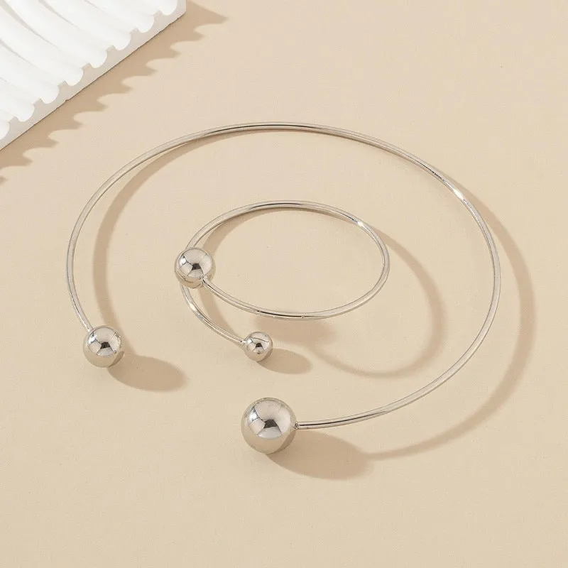 Gold dislocation ball open-end thin bangle bracelet with matching necklace on a flat surface