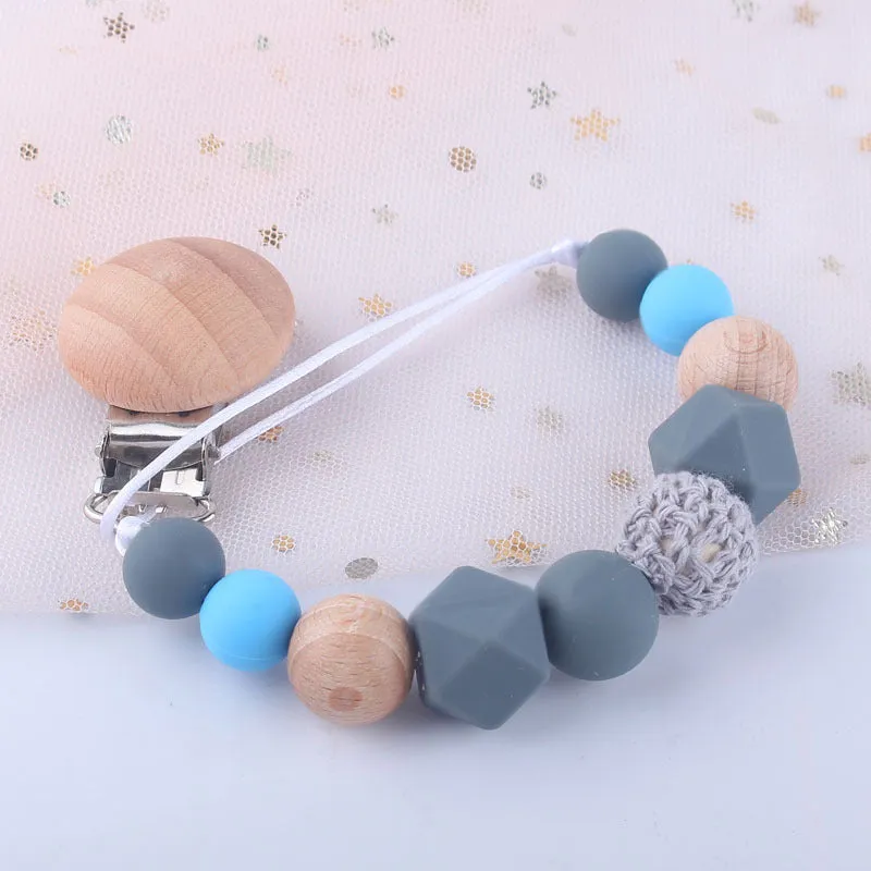 Baby silicone pacifier chain with beech wood beads in gradient colour, approximately 27cm long, clipped to a baby's clothing