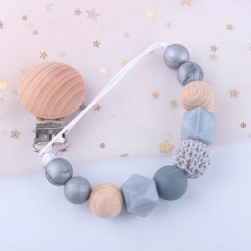 Baby silicone pacifier chain with beech wood beads in gradient colour, approximately 27cm long, clipped to a baby's clothing