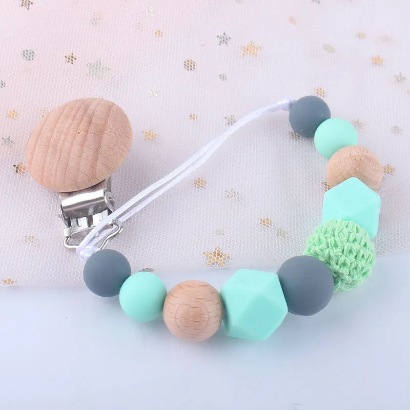 Baby silicone pacifier chain with beech wood beads in gradient colour, approximately 27cm long, clipped to a baby's clothing
