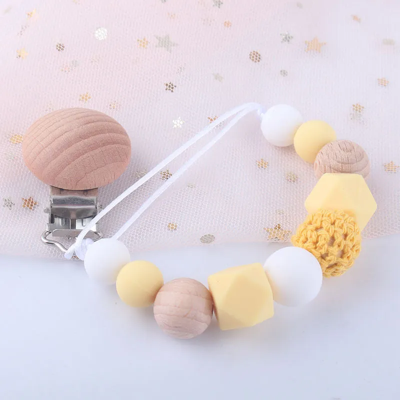 Baby silicone pacifier chain with beech wood beads in gradient colour, approximately 27cm long, clipped to a baby's clothing