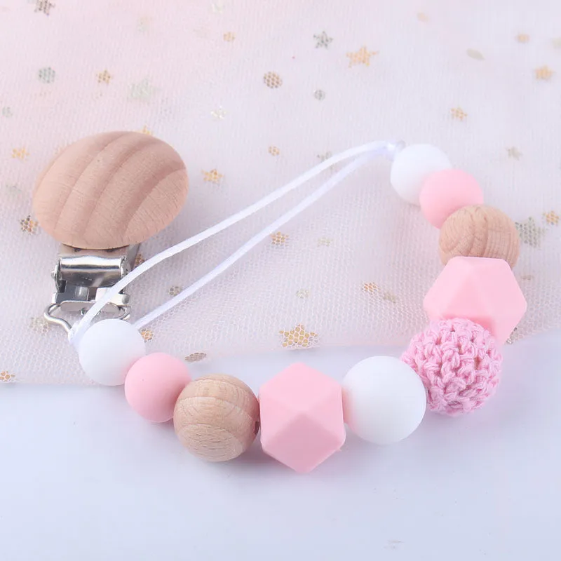Baby silicone pacifier chain with beech wood beads in gradient colour, approximately 27cm long, clipped to a baby's clothing