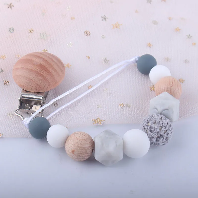 Baby silicone pacifier chain with beech wood beads in gradient colour, approximately 27cm long, clipped to a baby's clothing