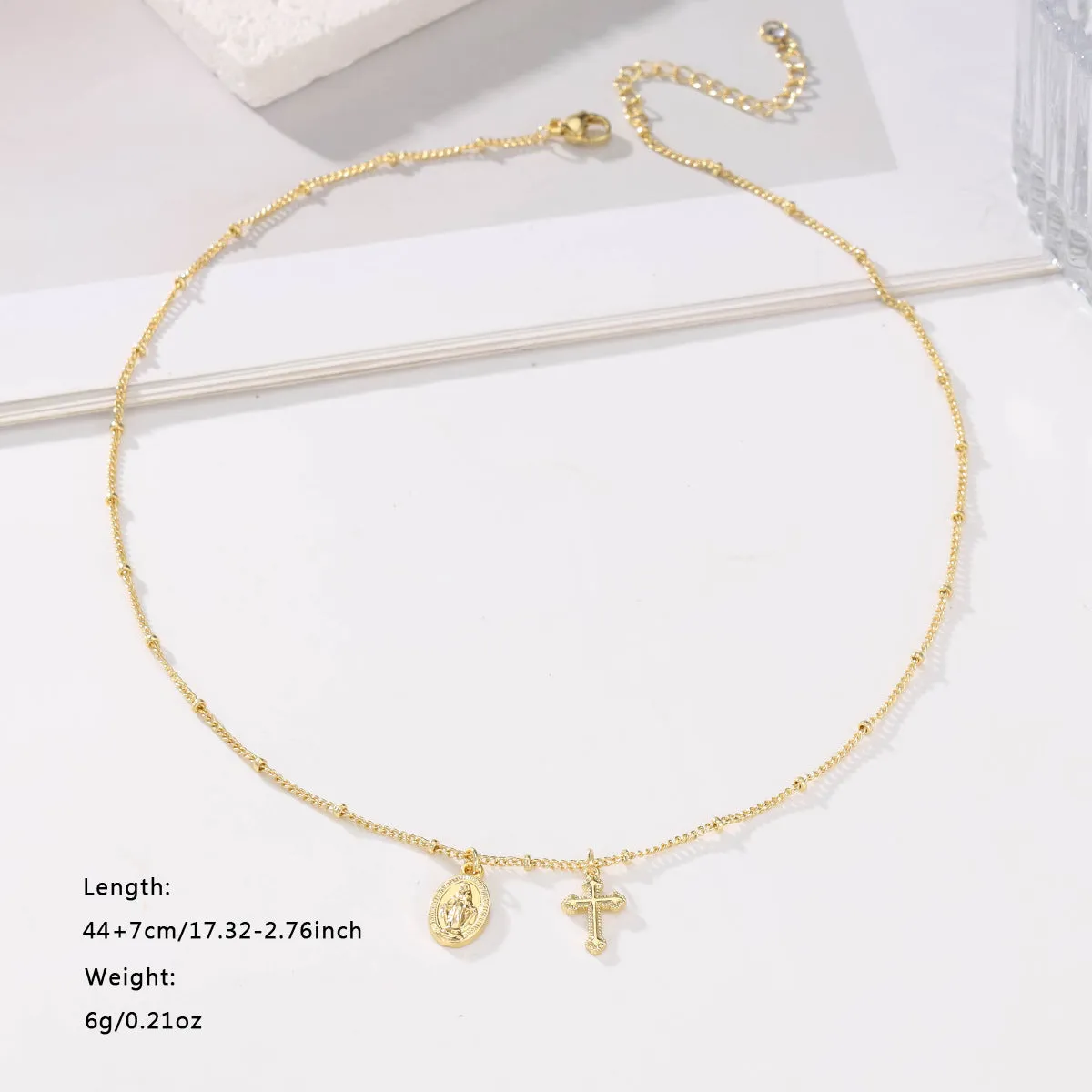 Gold coloured geometric cross necklace with a Virgin Mary ornament on a chain.