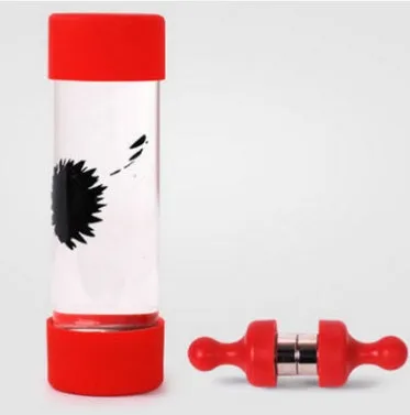 Magnetic fluid toy in a glass bottle with red ferrofluid and two black magnets on a white surface