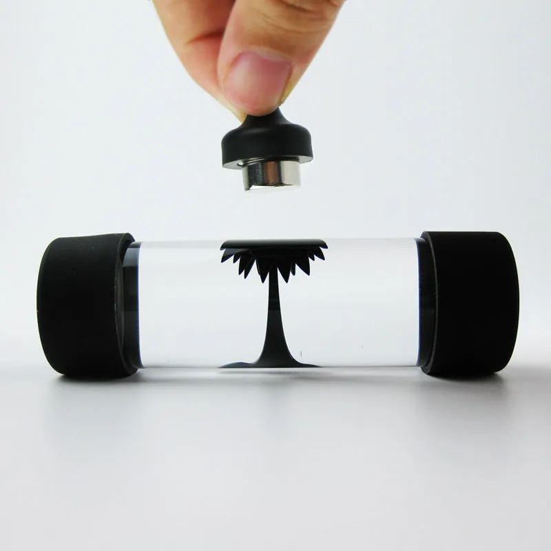 Magnetic fluid toy in a glass bottle with red ferrofluid and two black magnets on a white surface