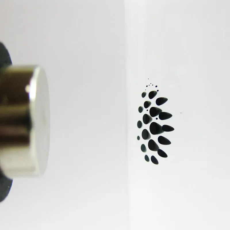 Magnetic fluid toy in a glass bottle with red ferrofluid and two black magnets on a white surface