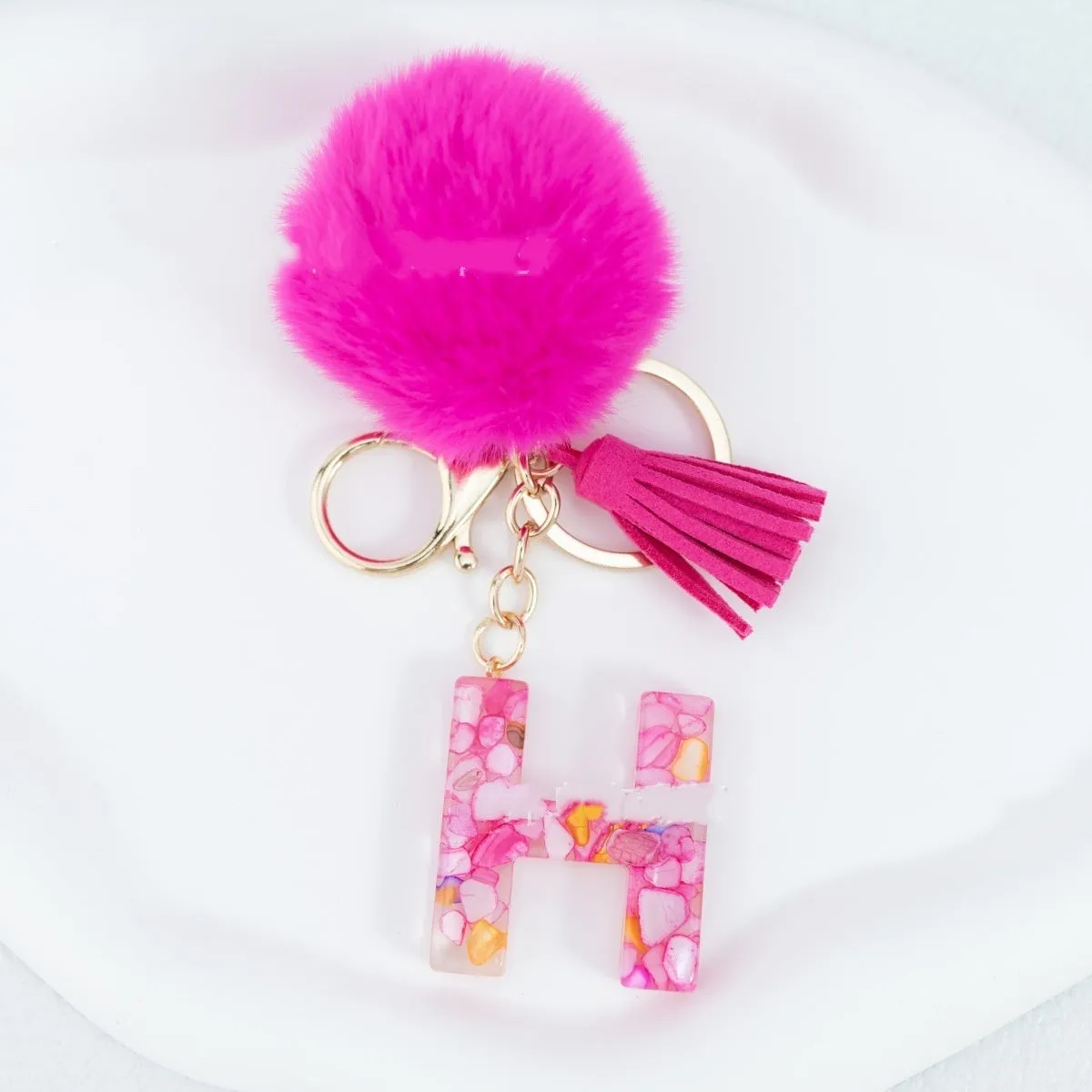Rose red stone keychain with English letter B, fur ball and tassel on a white background