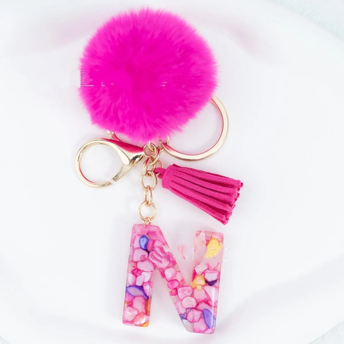 Rose red stone keychain with English letter B, fur ball and tassel on a white background