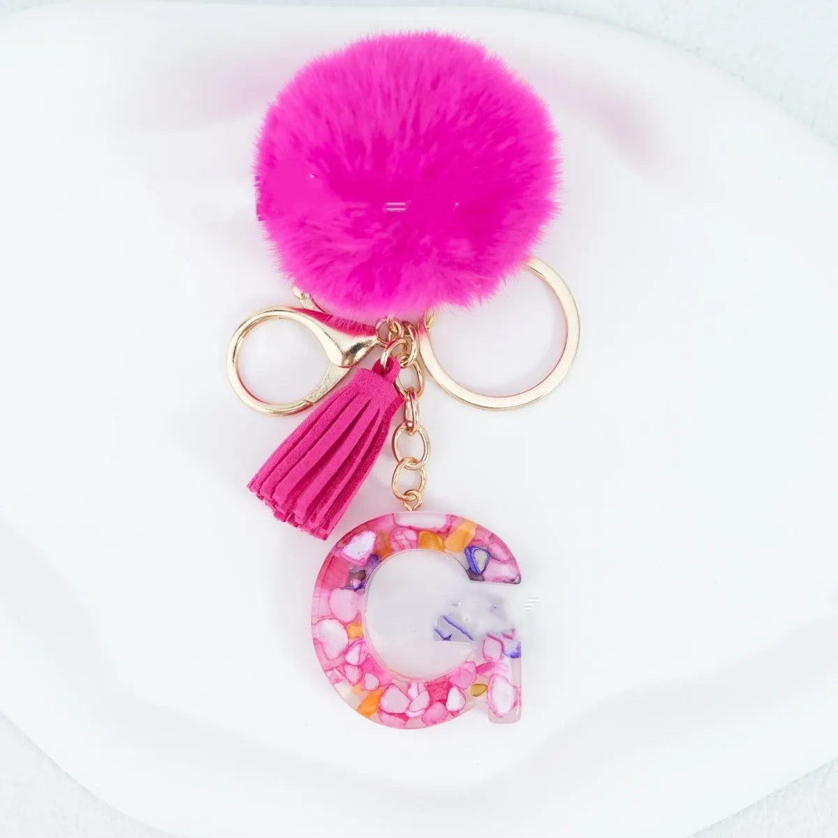 Rose red stone keychain with English letter B, fur ball and tassel on a white background