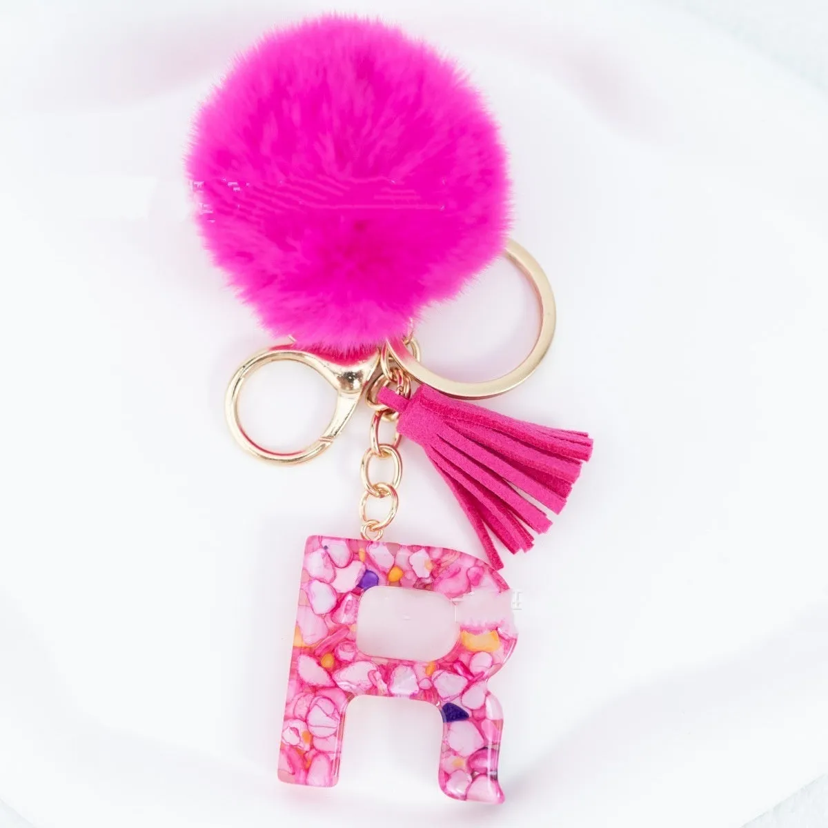 Rose red stone keychain with English letter B, fur ball and tassel on a white background