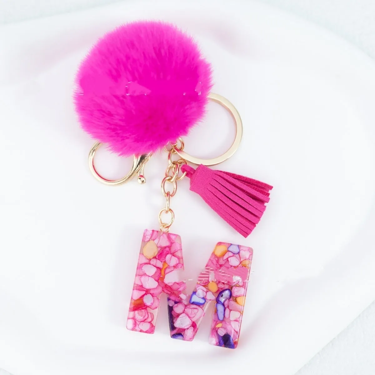 Rose red stone keychain with English letter B, fur ball and tassel on a white background