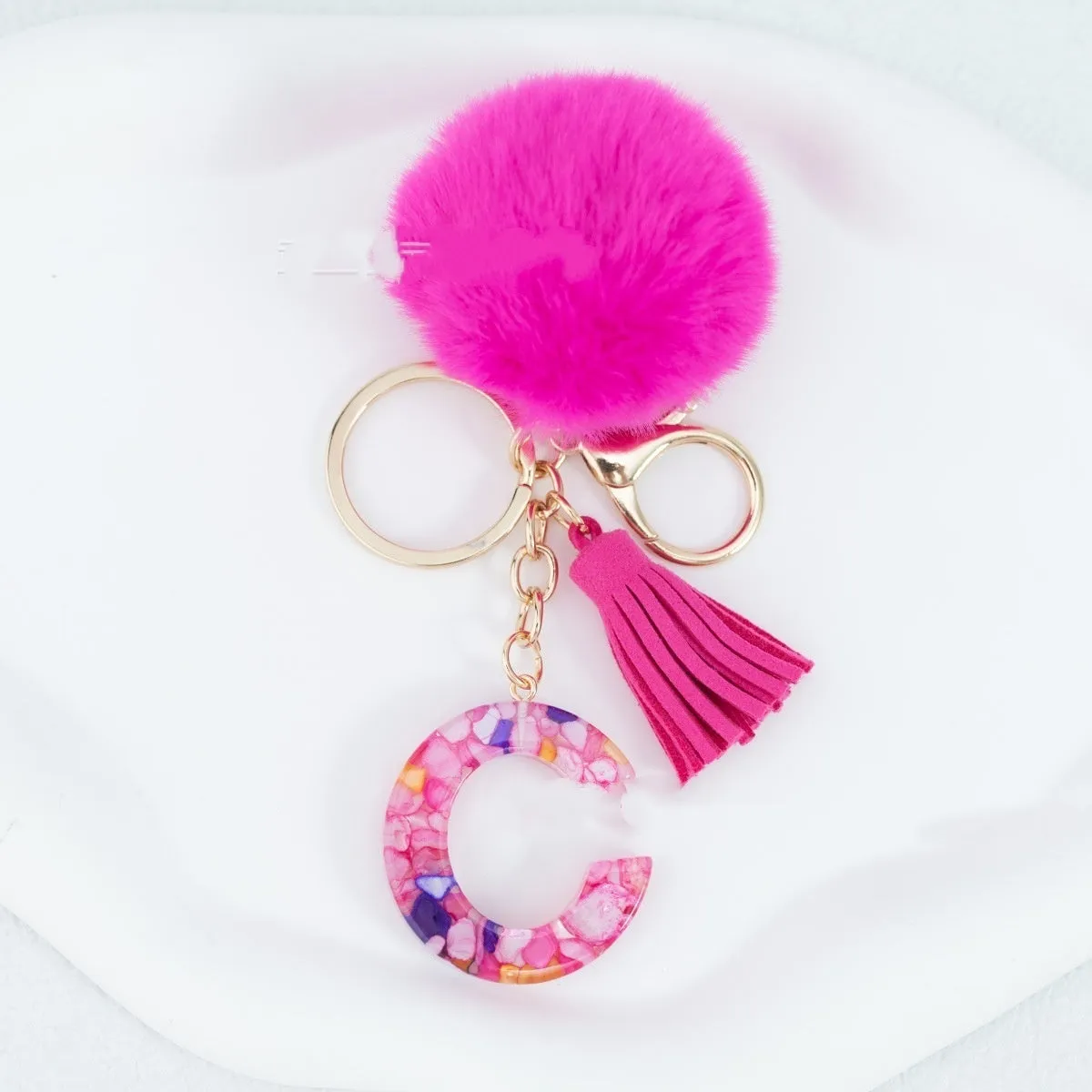 Rose red stone keychain with English letter B, fur ball and tassel on a white background