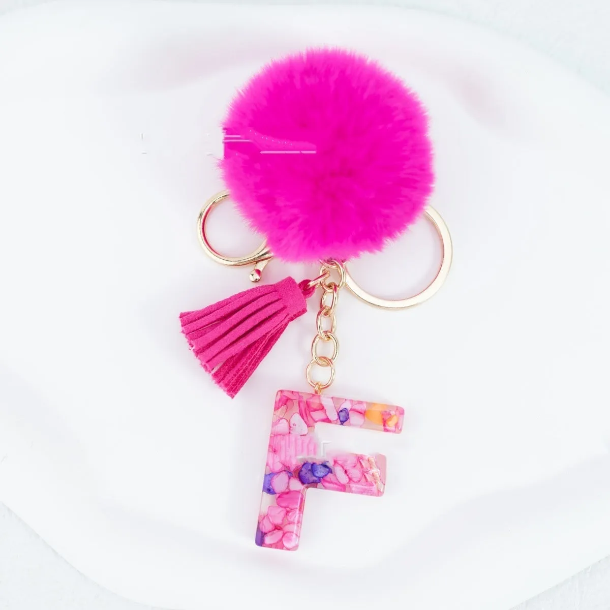 Rose red stone keychain with English letter B, fur ball and tassel on a white background