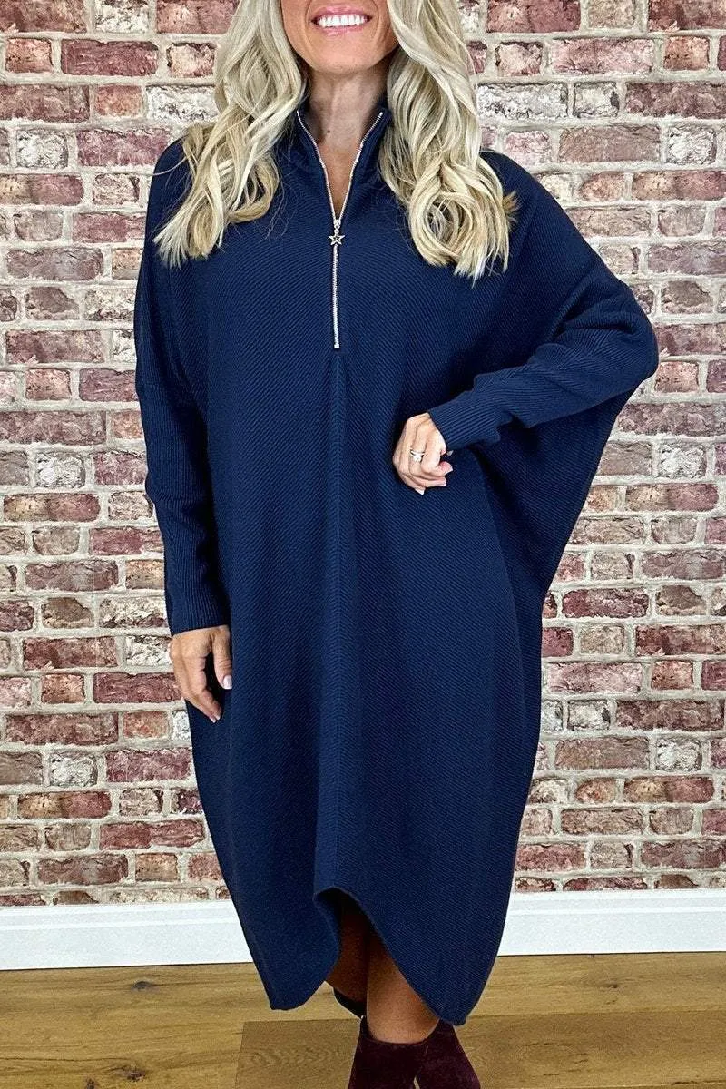 A woman wearing a solid dark green loose-fit knitted dress with raglan sleeves and a zipper detail.