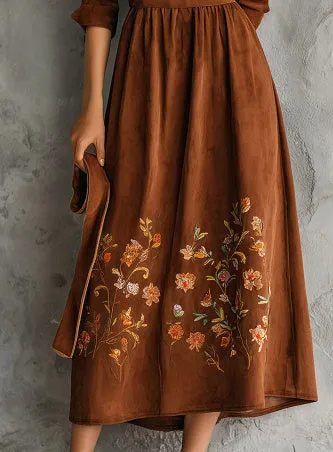 Brown suede-look midi dress with detailed floral embroidery on the bodice and hem, featuring three-quarter sleeves.