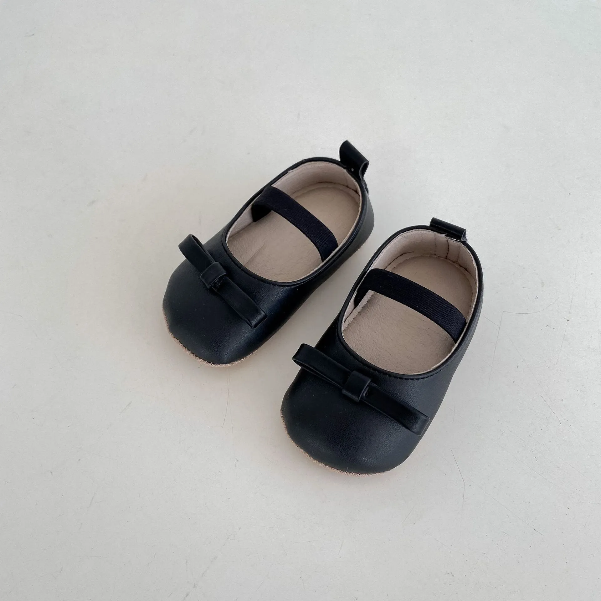 Women's soft non-slip PU low top baby shoes in black with bow detail on white background