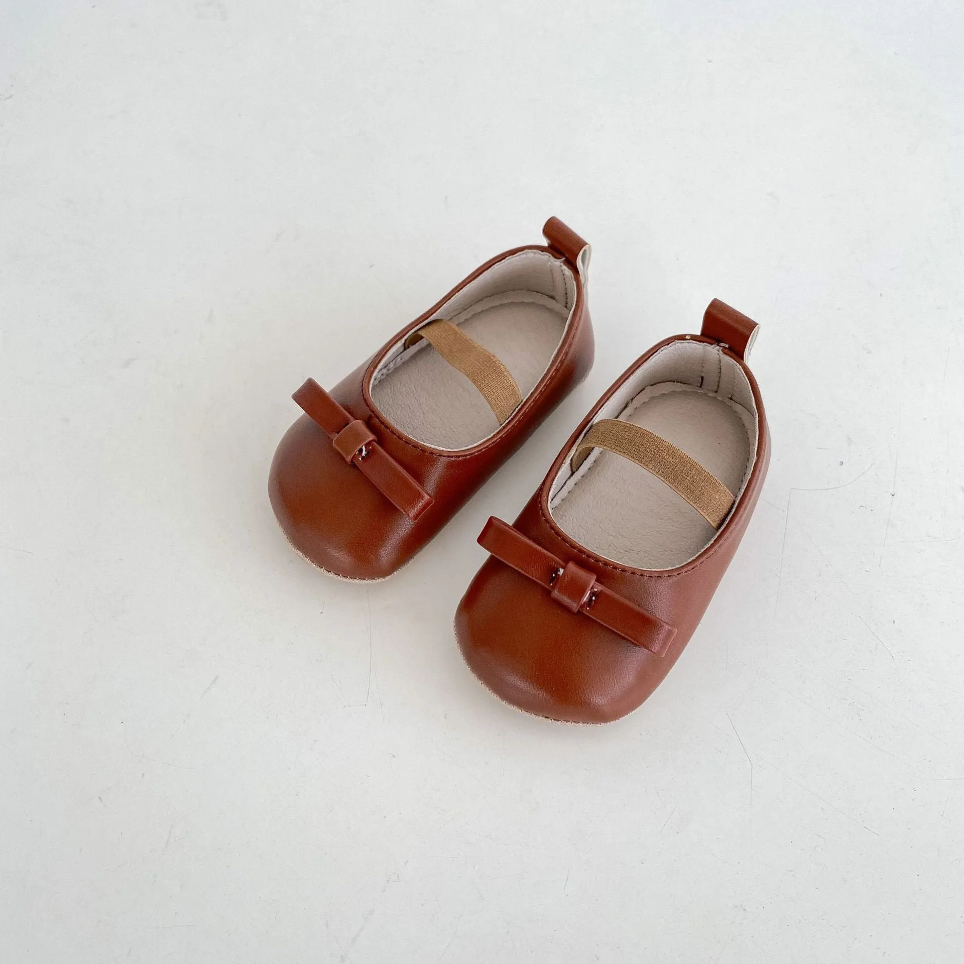 Women's soft non-slip PU low top baby shoes in black with bow detail on white background