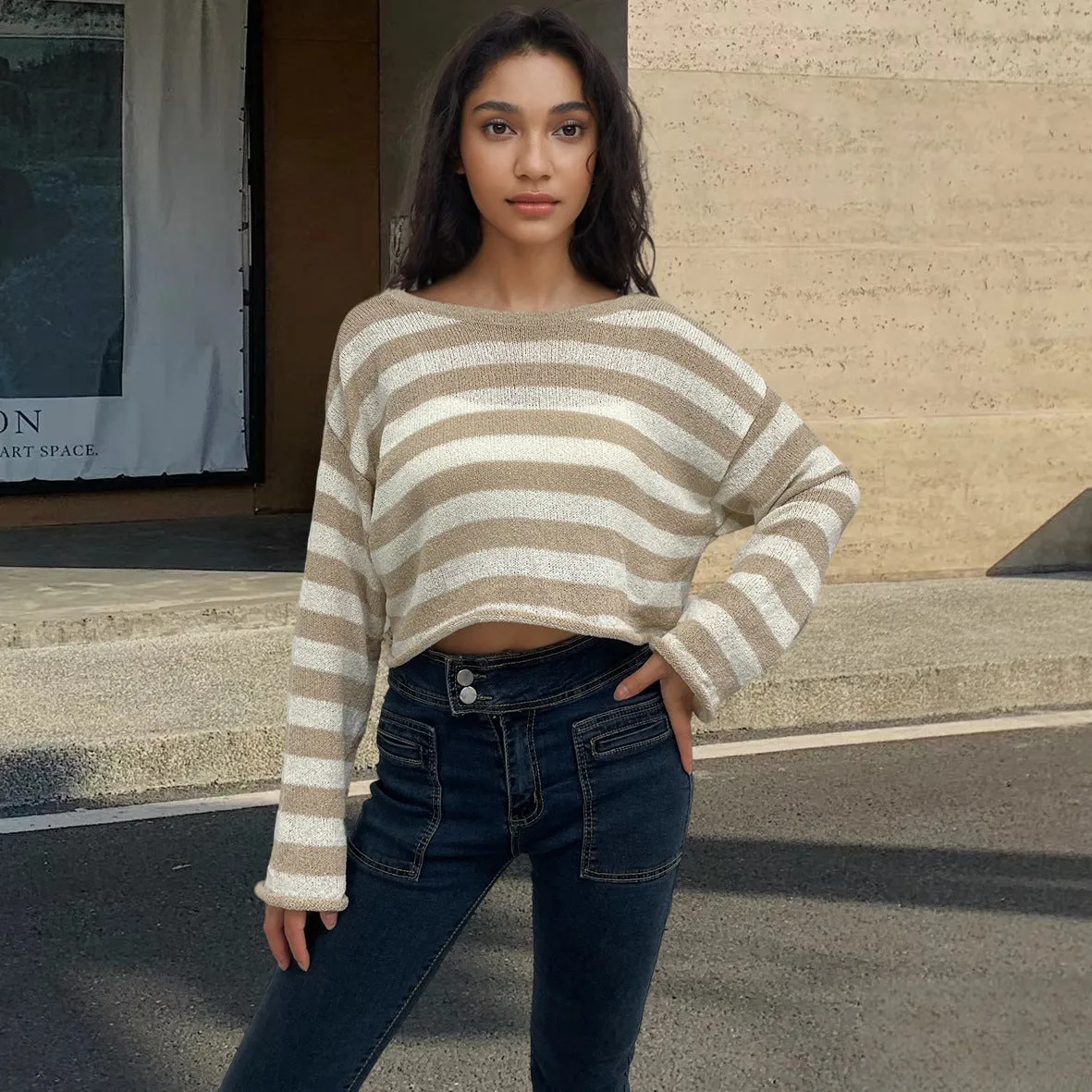 A woman wearing a cropped black and white striped long-sleeved sweater with a front and back exposed-navel design.